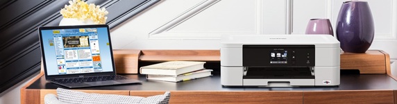 Skrivbord med öppen laptop, böcker, vit skrivare och dekor med lila vaser och gul blomma